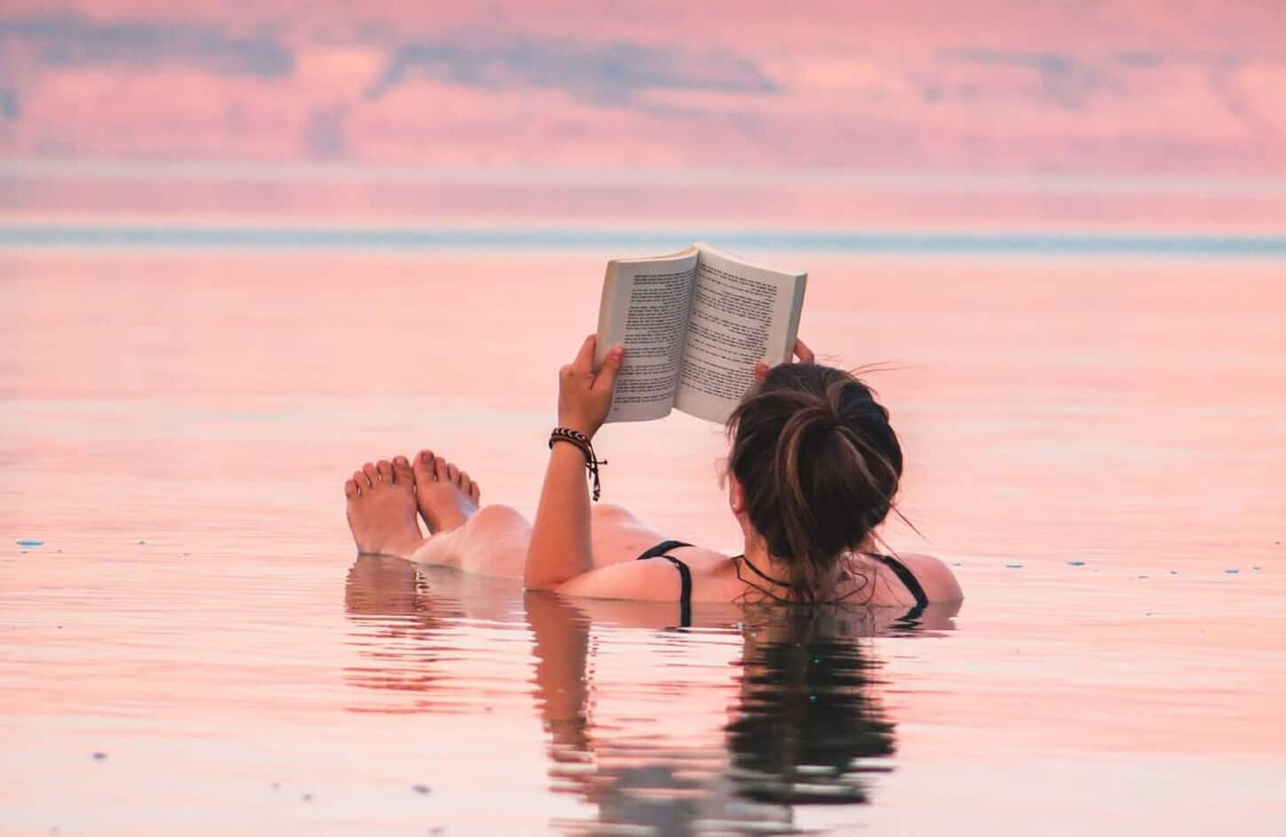 Tourist effortlessly floating while reading a book in the mineral-rich waters of the Dead Sea, Jordan