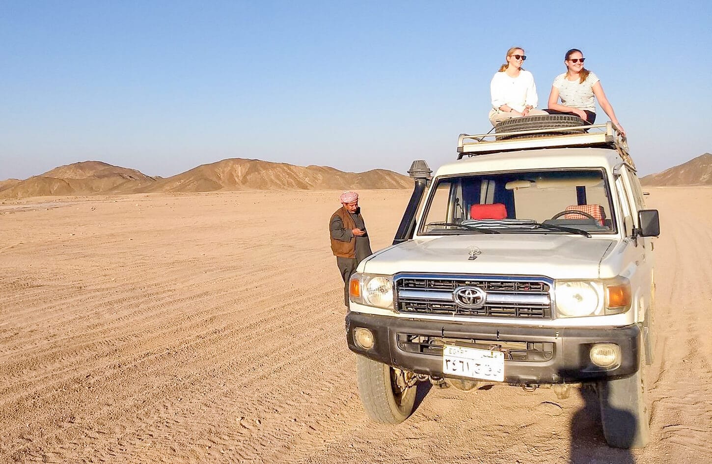 A wonderful shot of two girls sitting on a four wheel drive vehicle from a safari trip - Egypt Desert Safari Tours
