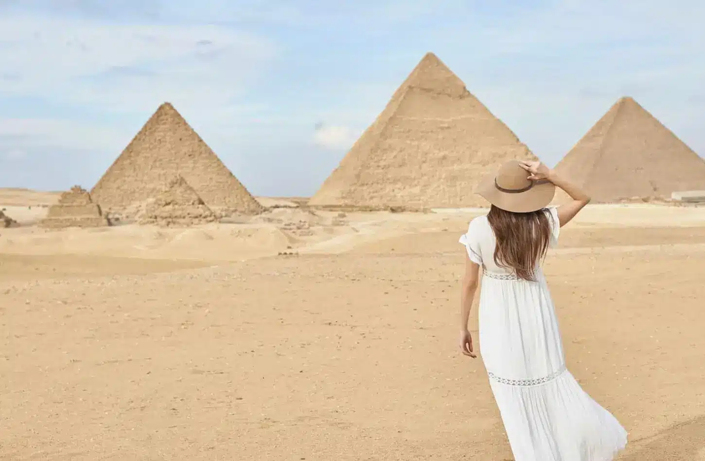 How to Plan an Egypt Tour on a Budget (Real Costs & Tips 2026) 1 A woman in a sun hat standing in the desert facing the Great Pyramids of Giza, representing how to plan an Egypt tour on a budget.