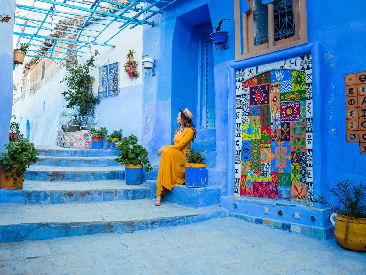 Very beautiful picture of a woman wearing a dress and a hat in the blue city of Chefchaouen
