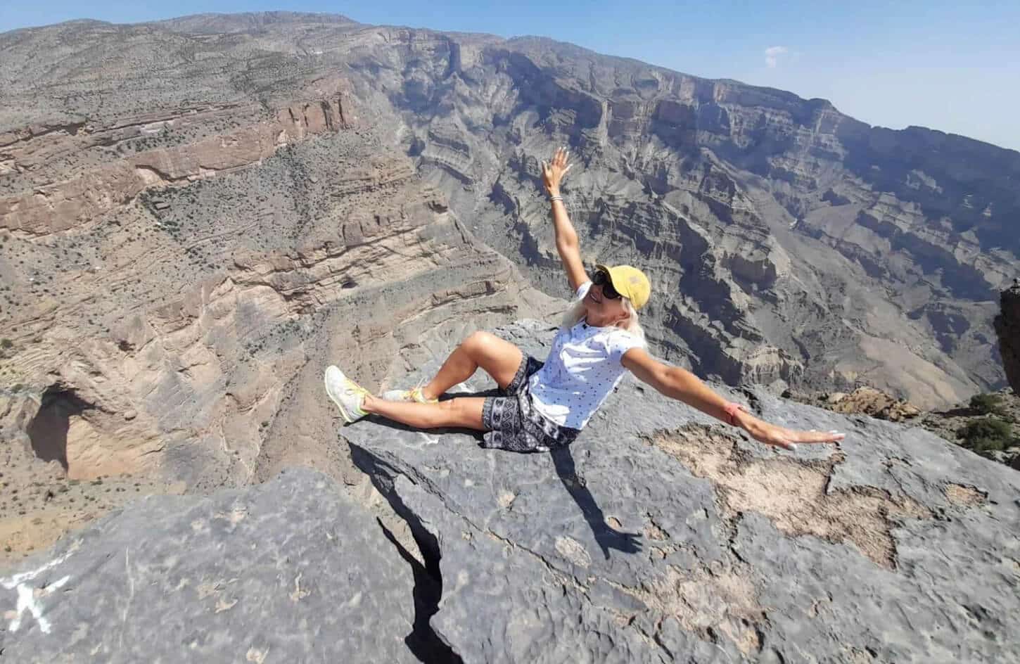 Woman traveler sitting on a cliff overlooking Jebel Shams mountain canyon in Oman