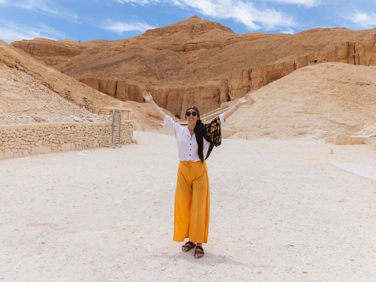 A woman stands in the Valley of the Kings, Luxor, surrounded by desert mountains and limestone cliffs.