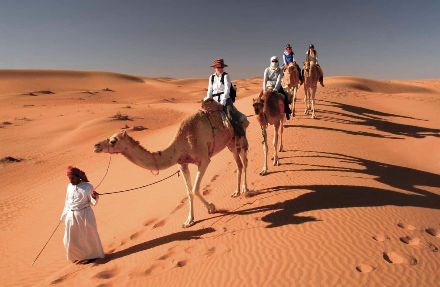 a great shot of some visitors riding camels at wahiba sands in oman
