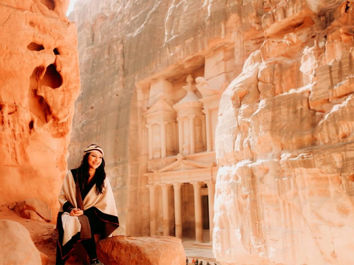 Tourist girl sitting in the Petra Siq, with the famous Al-Khazneh (The Treasury) facade of Jordan visible.