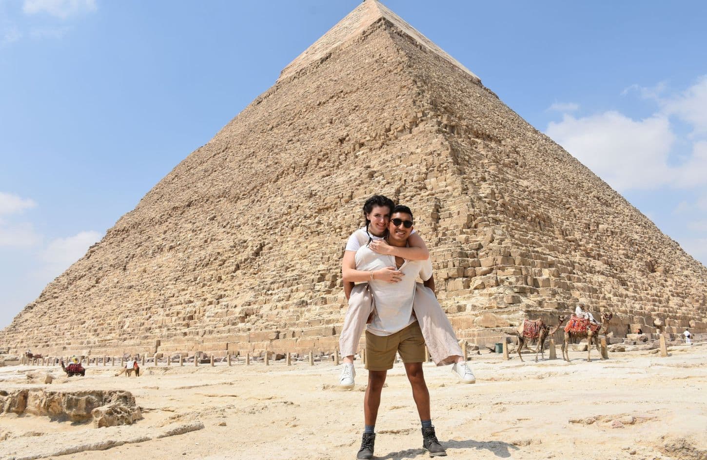 a wonderful shot of a husband carrying his wife on his back in front of the giza pyramids