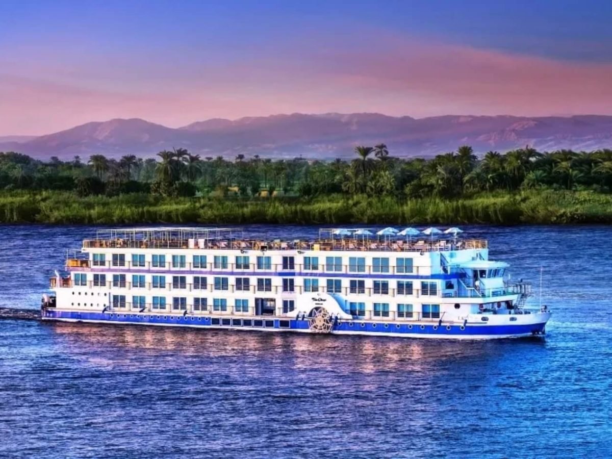 a large cruise ship sailing along the nile with lush greenery and mountains in the background