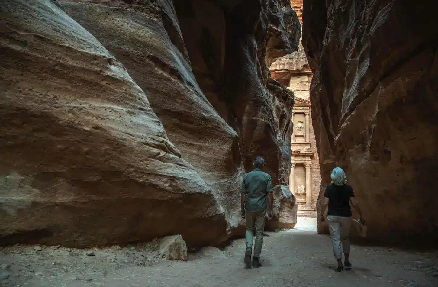 Best Time to Visit Jordan featuring two tourists walking through the narrow Siq canyon toward Al-Khazneh (The Treasury) in Petra