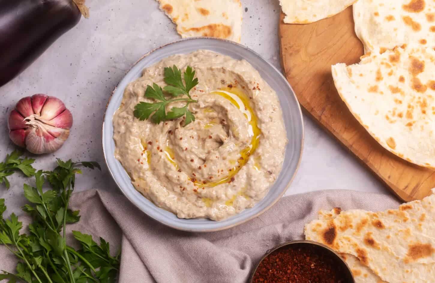 Smoky Egyptian baba ganoush eggplant dip with tahini, olive oil, and parsley in a clay bowl