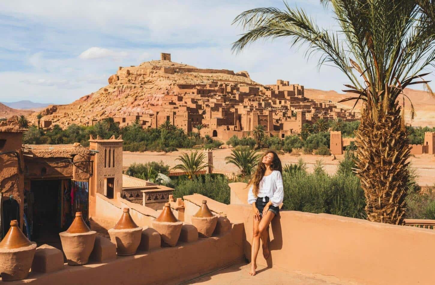 A woman relaxing under the sun with Ait Ben Haddou in the background, showing that it is safe to travel to Morocco and explore its beauty. - Is It Safe to Travel to Morocco in 2026? Complete Safety Guide