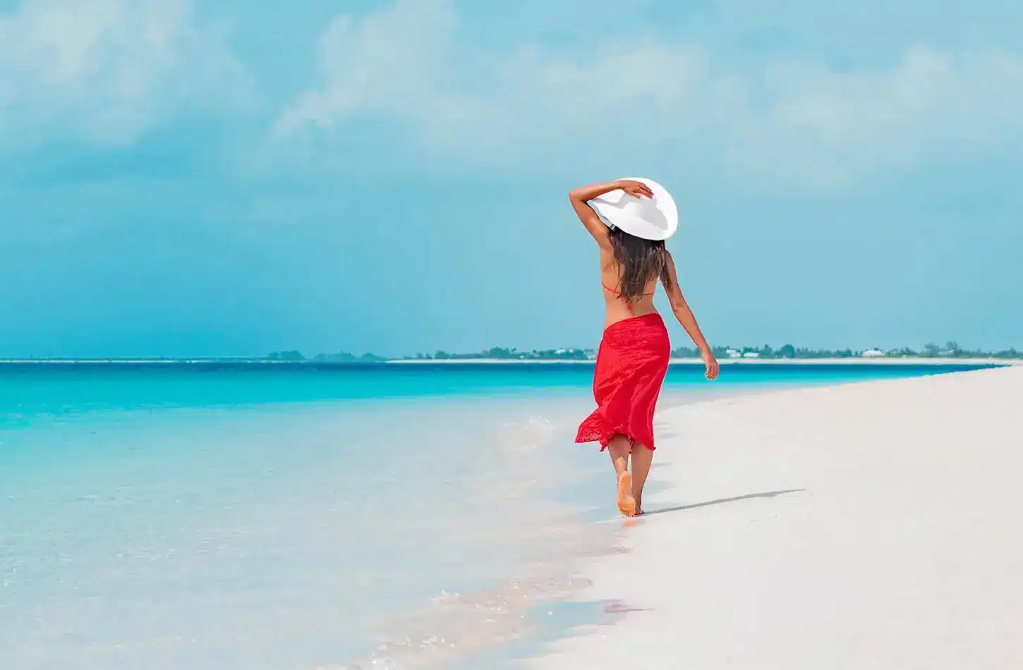 A woman in a red sarong walking on a white sand beach in Egypt during a luxury summer vacation. - Summer in Egypt 2026: The Honest Local Guide to June, July & August
