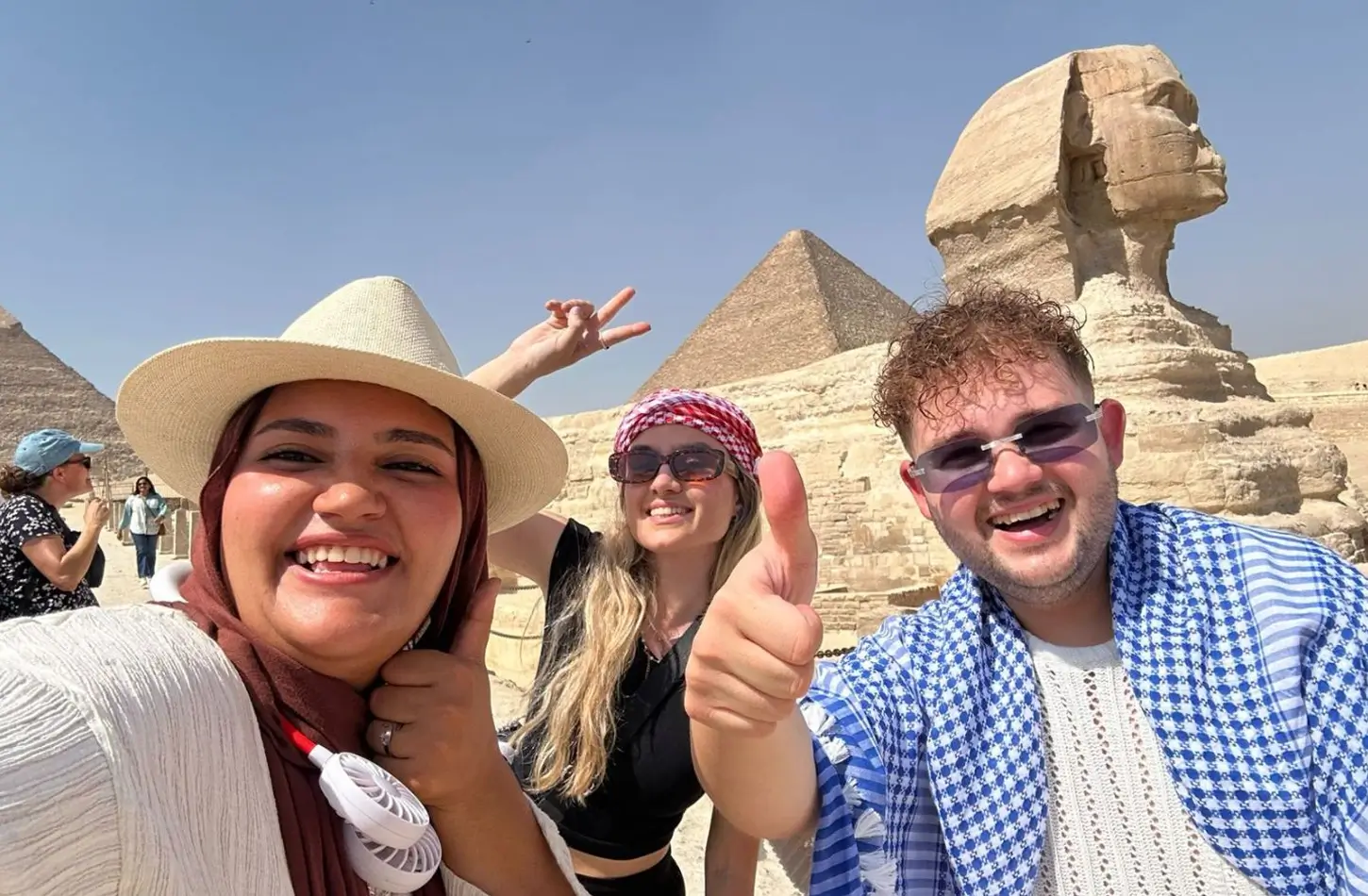Three smiling people posing for a selfie in front of the Sphinx and ancient Egyptian pyramids in the desert. - Do You Need a Tour Guide in Egypt? Here's the Honest Answer