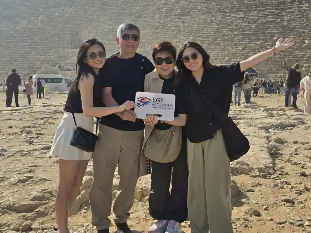 A family on a guided tour in Egypt posing with an Egy Vacations sign at the Great Pyramid of Giza. - Do You Need a Tour Guide in Egypt? Here's the Honest Answer