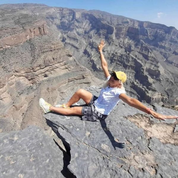 Woman traveler sitting on a cliff overlooking Jebel Shams mountain canyon in Oman